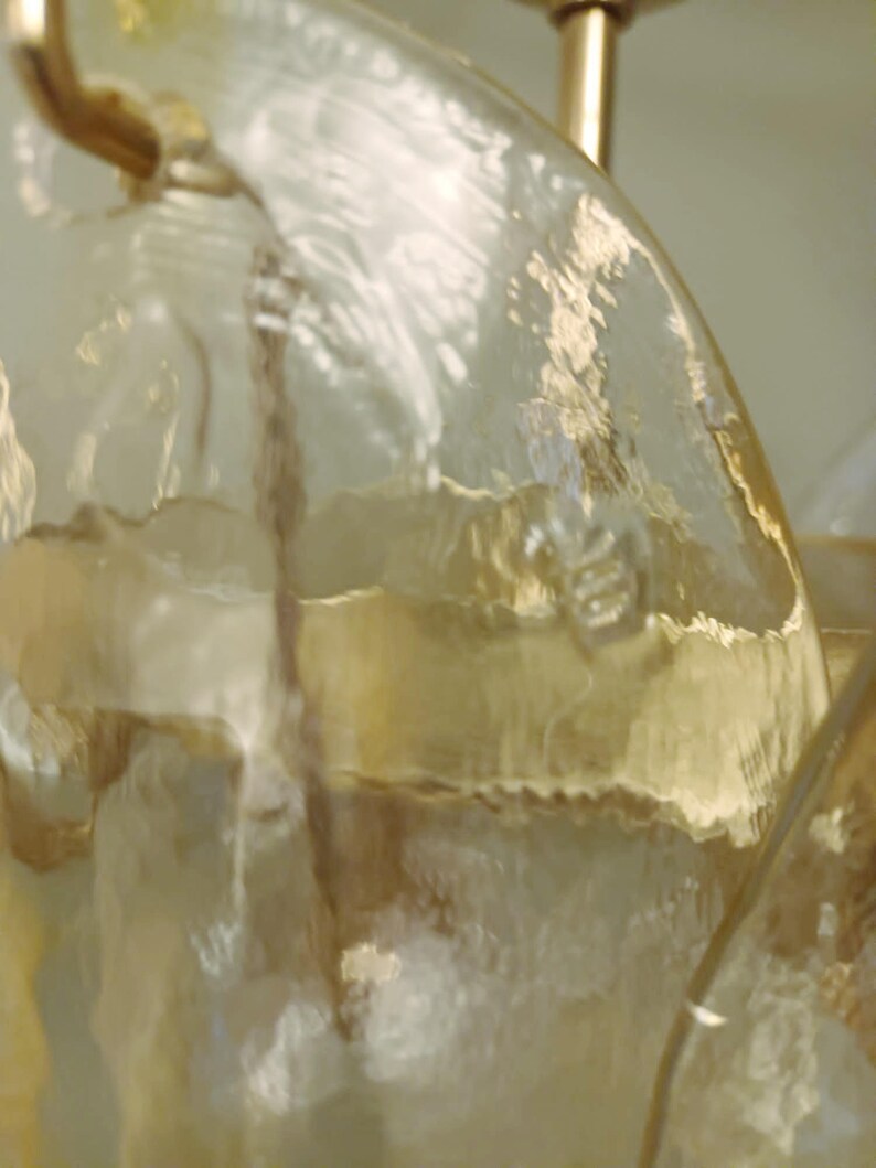 May include: Close-up of a clear glass chandelier with a textured surface. The glass has a yellowish tint and is attached to a gold-colored metal frame. The light fixture is likely for home decor.