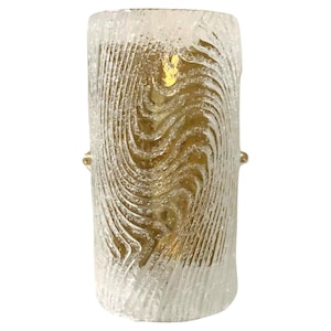 May include: A cylindrical glass wall sconce with a textured, wavy pattern. The glass is clear with a slight amber hue. The sconce has a gold metal base.