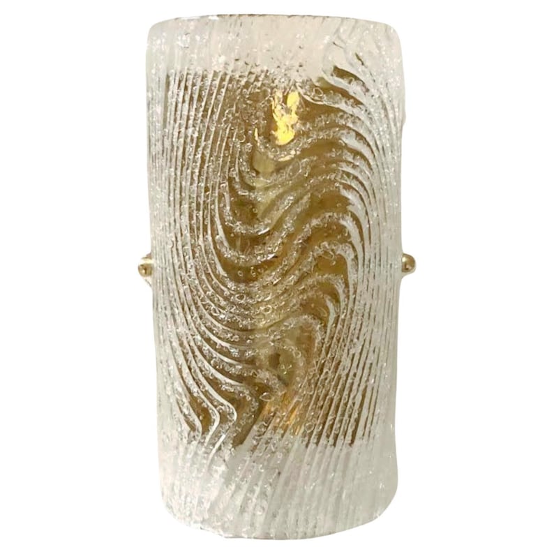 May include: A cylindrical glass wall sconce with a textured, wavy pattern. The glass is clear with a slight amber hue. The sconce has a gold metal base.