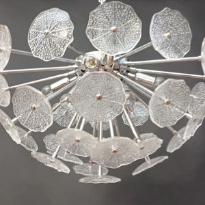 May include: A chrome and glass chandelier with multiple clear glass flower-shaped shades. The chandelier has a modern design and is perfect for a contemporary home.