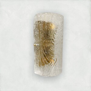 May include: A clear glass wall sconce with a textured, rippled pattern. The sconce has a gold metal backing and a single light bulb.