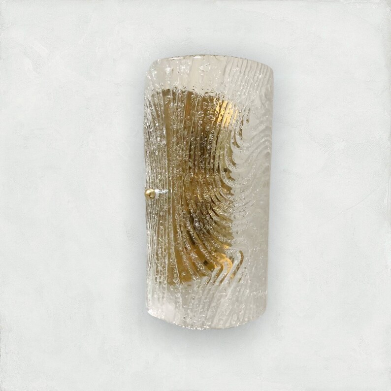 May include: A clear glass wall sconce with a textured, rippled pattern. The sconce has a gold metal backing and a single light bulb.