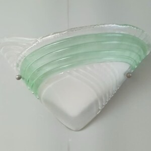 May include: A white and green glass wall sconce with a geometric design. The sconce has a triangular shape with a curved, layered green glass design on top.