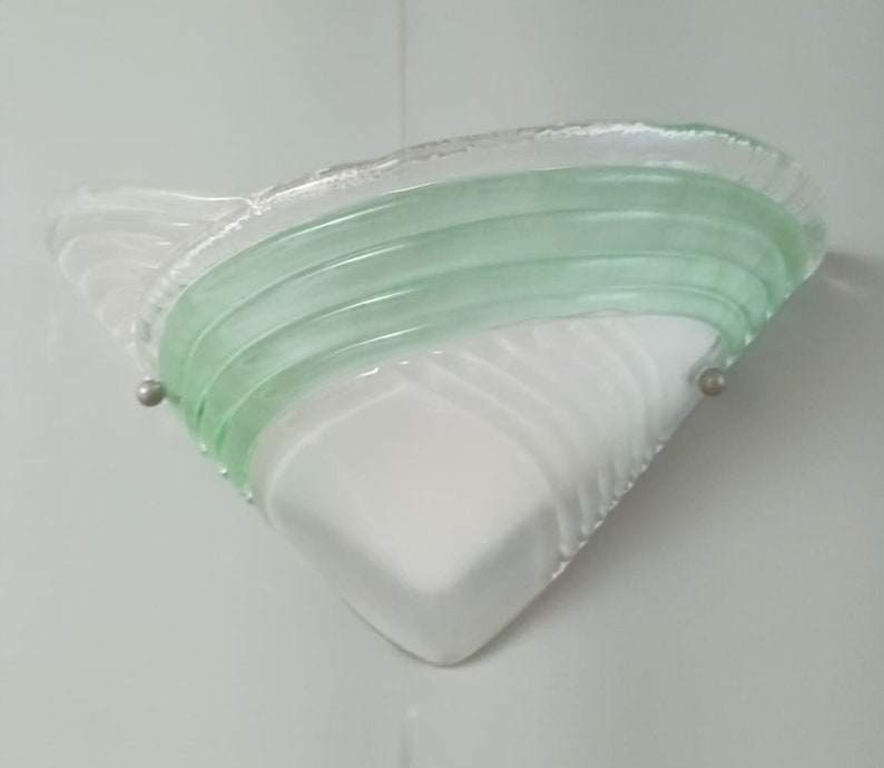 May include: A white and green glass wall sconce with a geometric design. The sconce has a triangular shape with a curved, layered green glass design on top.