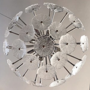 May include: A chrome and glass chandelier with multiple clear glass shades in a flower shape. The chandelier has a modern design and is perfect for a contemporary home.