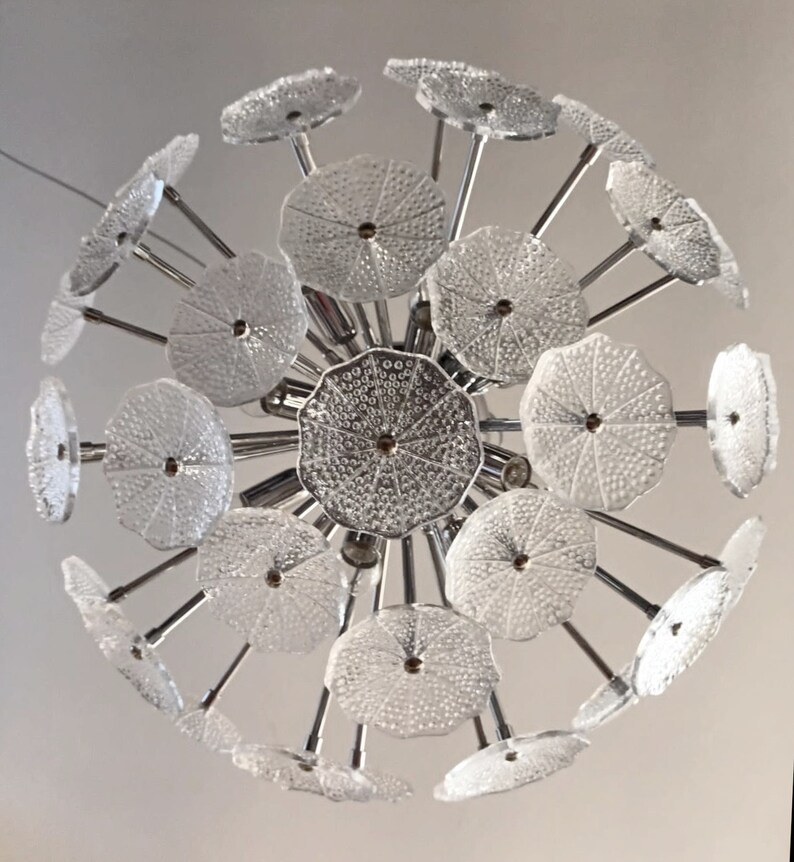 May include: A chrome and glass chandelier with multiple clear glass shades in a flower shape. The chandelier has a modern design and is perfect for a contemporary home.