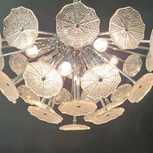 May include: A large, modern chandelier with multiple clear glass shades in a flower shape. The chandelier has a chrome finish and is lit by multiple light bulbs.