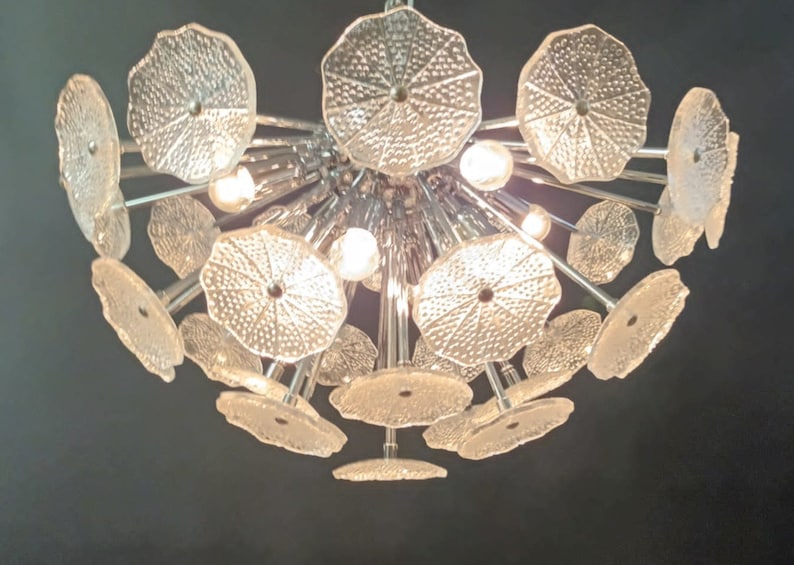 May include: A large, modern chandelier with multiple clear glass shades in a flower shape. The chandelier has a chrome finish and is lit by multiple light bulbs.