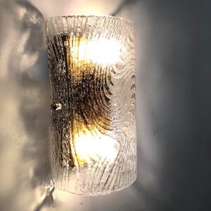 May include: A clear glass wall sconce with a textured, wavy pattern. The sconce has a brass backing and two light bulbs.