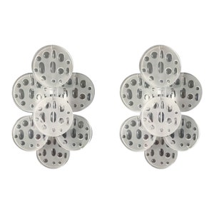 May include: A pair of clear acrylic earrings with a flower-like design. Each earring is made up of five overlapping circles with a textured surface.