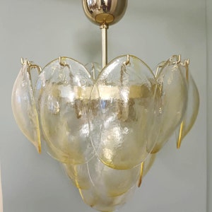 May include: A vintage-style chandelier with a gold-toned metal frame and multiple tiers of textured, petal-shaped glass shades. The glass has a soft yellow hue, creating a warm, inviting glow. The fixture is suspended from a matching gold ceiling mount.