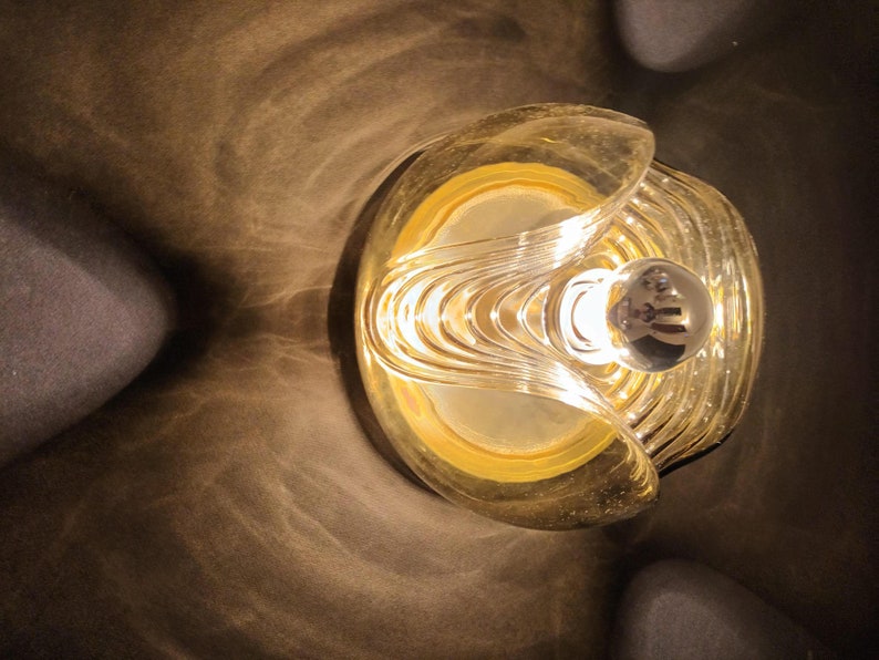 Puede incluir: Una l&aacute;mpara de techo dorada con una pantalla de vidrio transparente y un patr&oacute;n geom&eacute;trico decorativo. La luz est&aacute; encendida y proyecta un brillo c&aacute;lido.