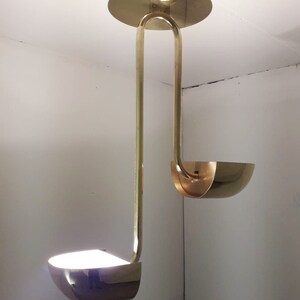 May include: A gold-toned pendant light fixture with two curved shades. The fixture is suspended from the ceiling by a single rod.