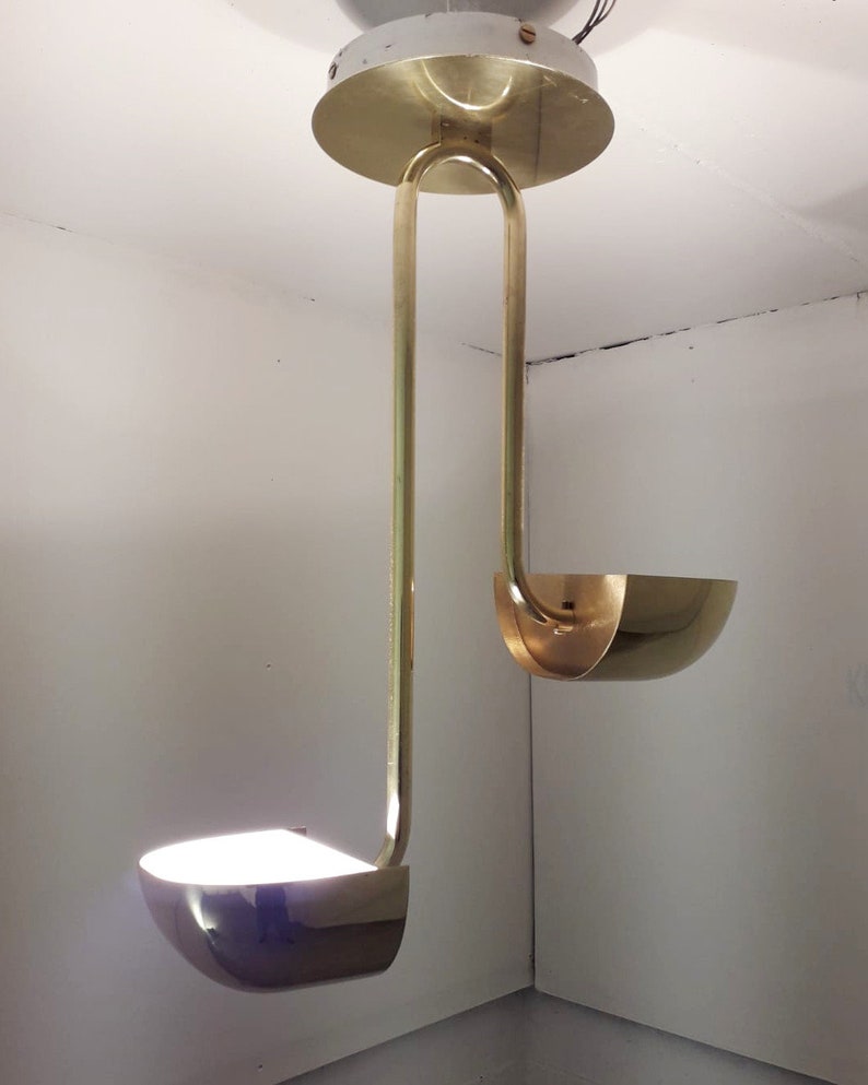 May include: A gold-toned pendant light fixture with two curved shades. The fixture is suspended from the ceiling by a single rod.