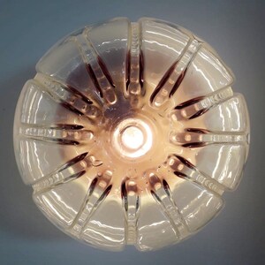Pu&ograve; includere: Un paralume in plastica trasparente con un design testurizzato e nervato. Il paralume &egrave; illuminato dall'interno, proiettando una luce calda.