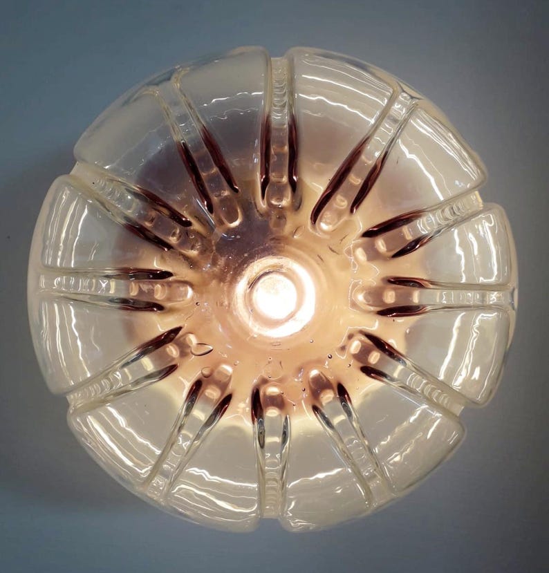 Pu&ograve; includere: Un paralume in plastica trasparente con un design testurizzato e nervato. Il paralume &egrave; illuminato dall'interno, proiettando una luce calda.