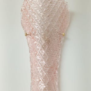 May include: A pink glass wall sconce with a textured diamond pattern. The sconce has a rounded top and a pointed bottom.