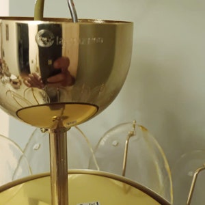 May include: A gold-colored, vintage-style chandelier with a floral design. The chandelier has a large, rounded top with a reflective surface, and clear, petal-shaped glass elements. The fixture is suspended by a gold-colored rod.
