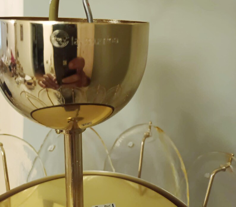 May include: A gold-colored, vintage-style chandelier with a floral design. The chandelier has a large, rounded top with a reflective surface, and clear, petal-shaped glass elements. The fixture is suspended by a gold-colored rod.