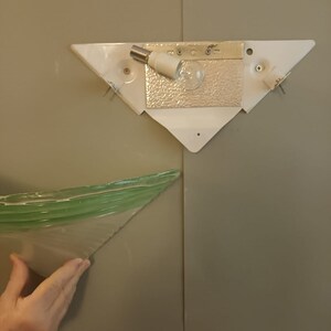 May include: A white triangular light fixture with a light bulb and a green glass shade.