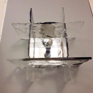 May include: A modern glass and metal ceiling light fixture with a geometric design. The light fixture has a clear glass shade with a silver metal base.