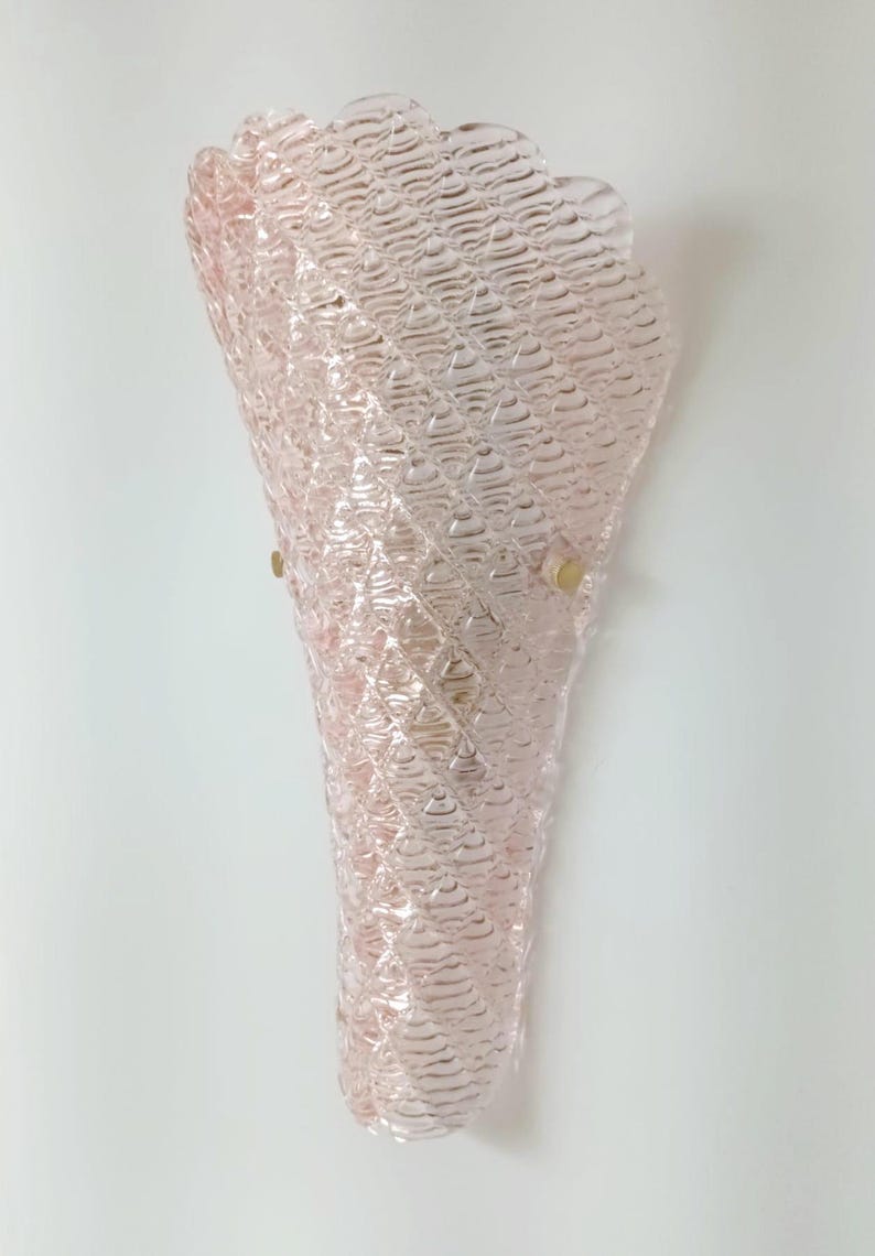 May include: A pink glass wall sconce with a textured, waffle-like pattern. The sconce has a cone shape and is mounted on a white wall.
