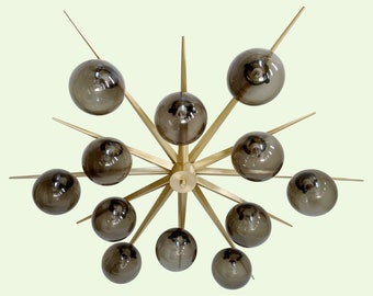 May include: A gold metal chandelier with 12 smoked glass globes. The chandelier has a starburst design with long, pointed arms.