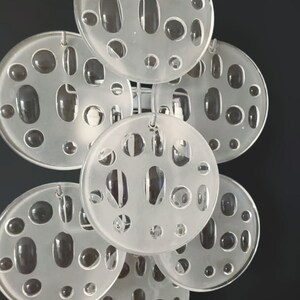 May include: A white frosted glass pendant light fixture with multiple circular discs, each with a pattern of small and large holes. The discs are connected by metal rods.