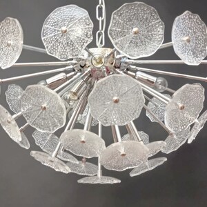 May include: A chrome chandelier with clear glass flower-shaped shades. The chandelier has a modern design and is perfect for a contemporary home.