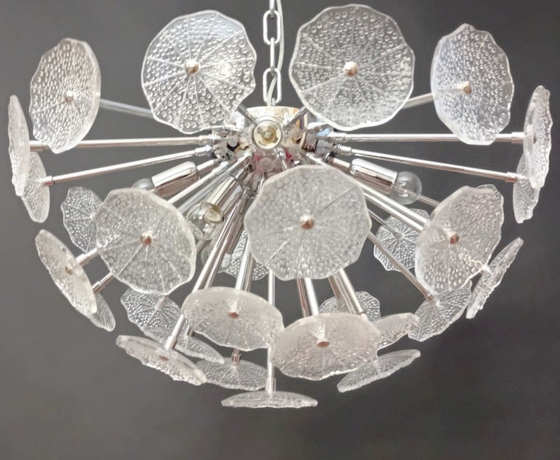 May include: A chrome chandelier with clear glass flower-shaped shades. The chandelier has a modern design and is perfect for a contemporary home.
