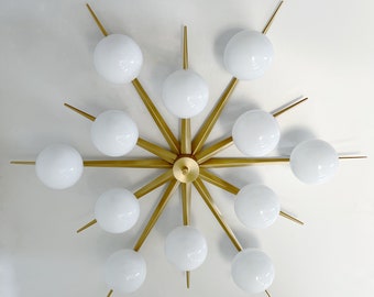 May include: A gold metal starburst chandelier with 12 white globe light bulbs. The chandelier has a modern design and is perfect for a contemporary home.