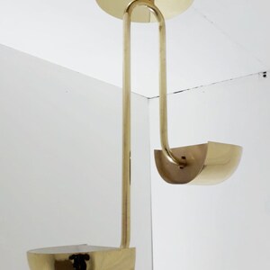 May include: A brass pendant light fixture with two curved shades. The fixture has a simple, modern design.