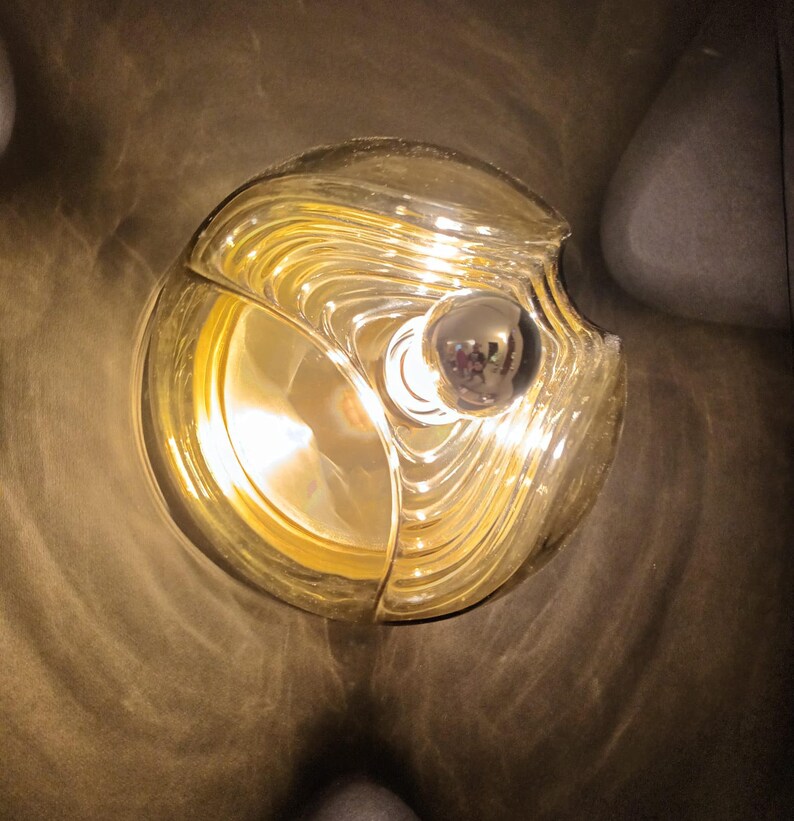 Puede incluir: Una l&aacute;mpara redonda de vidrio de color dorado con una bombilla en su interior. La l&aacute;mpara tiene un dise&ntilde;o &uacute;nico, ondulado y texturizado.
