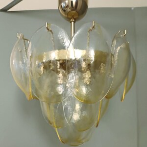 May include: A vintage chandelier with a gold-toned metal frame and clear, petal-shaped glass shades. The shades are layered, creating a floral design. The light fixture is suspended from a gold-colored ceiling mount.