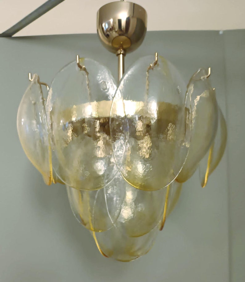 May include: A vintage chandelier with a gold-toned metal frame and clear, petal-shaped glass shades. The shades are layered, creating a floral design. The light fixture is suspended from a gold-colored ceiling mount.