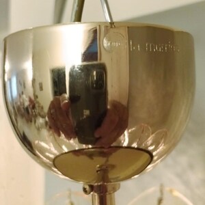 May include: A polished, metallic light fixture with a rounded, bowl-like shade. The surface reflects the surrounding environment, including a person holding a phone. The fixture has a decorative design and a central support rod.