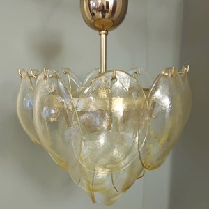 May include: A vintage chandelier with a gold-toned metal frame and a series of petal-shaped glass shades. The shades are a pale yellow color, and the fixture is suspended from a gold-colored ceiling mount.