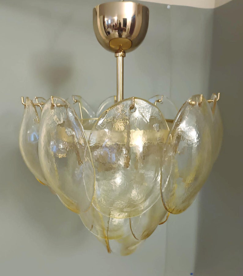 May include: A vintage chandelier with a gold-toned metal frame and a series of petal-shaped glass shades. The shades are a pale yellow color, and the fixture is suspended from a gold-colored ceiling mount.