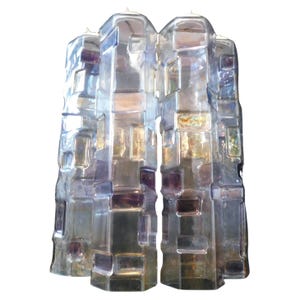 May include: Three clear glass candle holders with a textured, geometric design. The holders have a rectangular shape with purple and gold accents. These decorative candle holders are suitable for home decor.