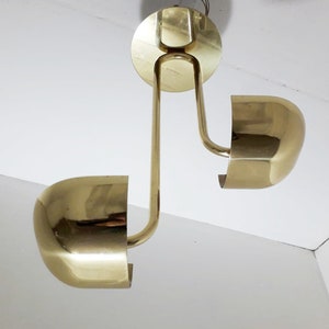 May include: A brass ceiling light fixture with two round shades. The fixture has a curved arm and a circular base.