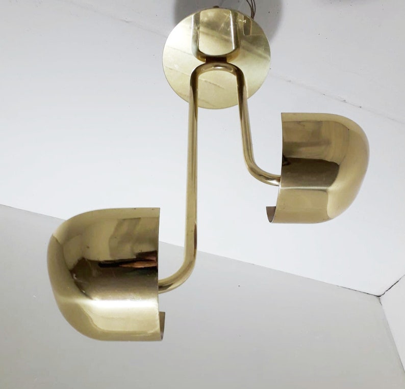 May include: A brass ceiling light fixture with two round shades. The fixture has a curved arm and a circular base.