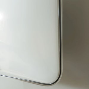May include: Close-up of the edge of a white, rectangular, framed mirror with a silver frame.