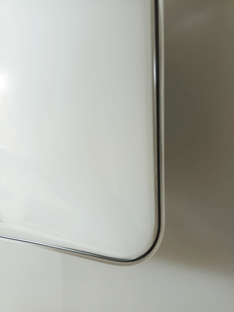 May include: Close-up of the edge of a white, rectangular, framed mirror with a silver frame.