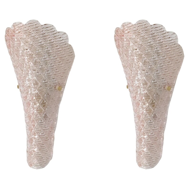 May include: A pair of pink glass wall sconces with a textured, woven design. The sconces have a scalloped edge and a brass mounting.