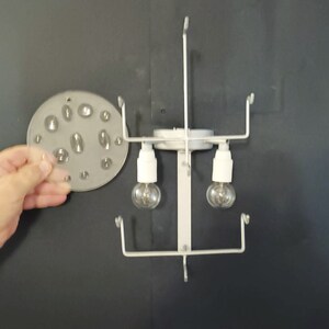 May include: White metal light fixture with two clear light bulbs and a round, clear plastic diffuser with multiple small holes.