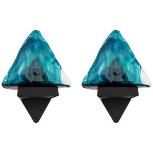 May include: A pair of wall sconces with teal blue glass shades. The shades are shaped like a triangle and have a swirling pattern. The sconces have black metal bases.