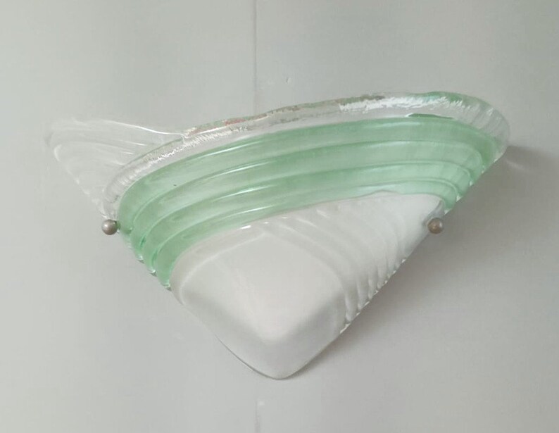 May include: A white and green glass wall sconce with a triangular shape and a wavy design. The sconce has a green glass band with a wavy design.