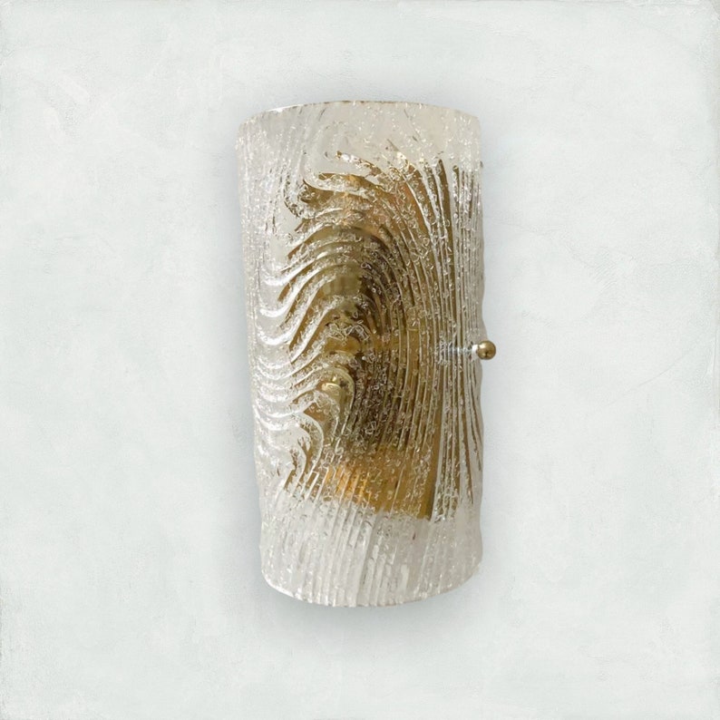 May include: A cylindrical glass wall sconce with a textured, rippled pattern. The sconce has a gold finish and a single light bulb.