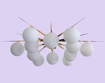 May include: A gold-toned metal chandelier with a starburst design and 10 white frosted glass globes.