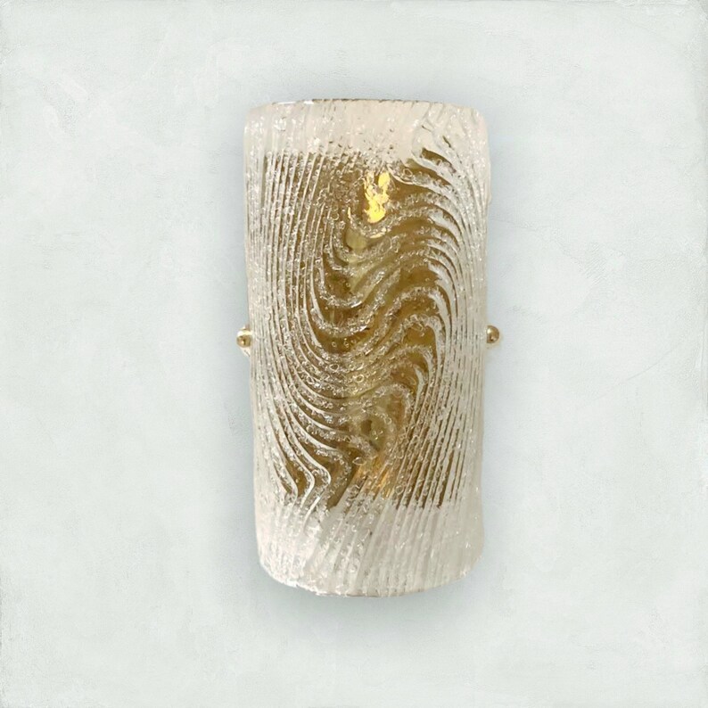 May include: A gold-toned wall sconce with a clear glass shade featuring a swirling, textured pattern.